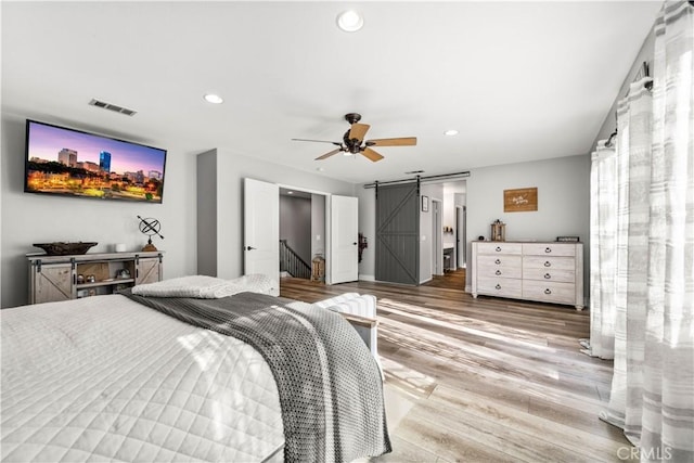 bedroom featuring ceiling fan, a barn door, and wood-type flooring