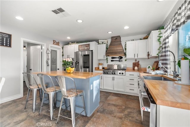 kitchen with premium range hood, a center island, white cabinetry, stainless steel fridge, and butcher block counters