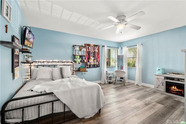 bedroom featuring ceiling fan, light hardwood / wood-style flooring, and a fireplace