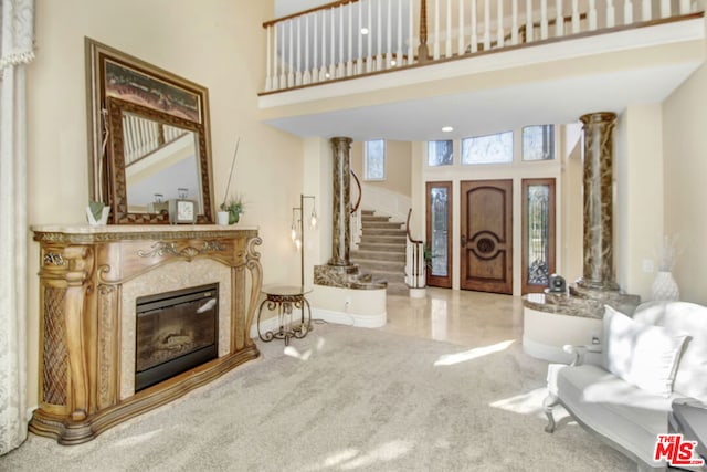 carpeted entrance foyer with decorative columns, a premium fireplace, and a towering ceiling