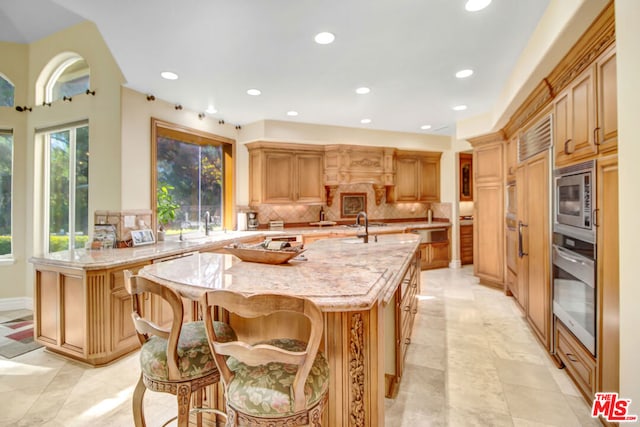 kitchen featuring appliances with stainless steel finishes, decorative backsplash, a kitchen breakfast bar, a kitchen island with sink, and light stone counters