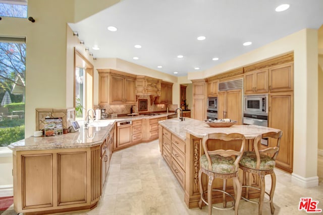 kitchen with built in appliances, sink, kitchen peninsula, light stone counters, and a breakfast bar