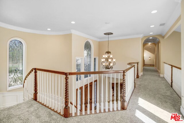 hall with plenty of natural light, light colored carpet, crown molding, and a notable chandelier