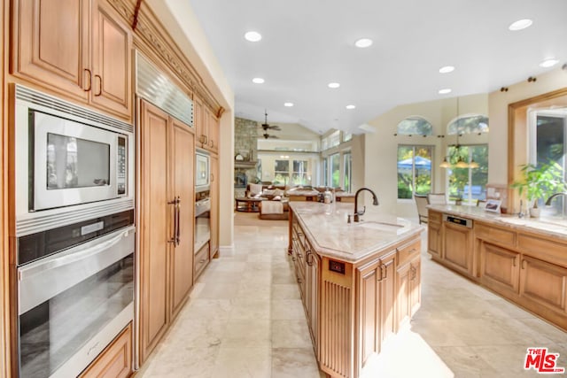 kitchen with ceiling fan, sink, an island with sink, a stone fireplace, and stainless steel appliances