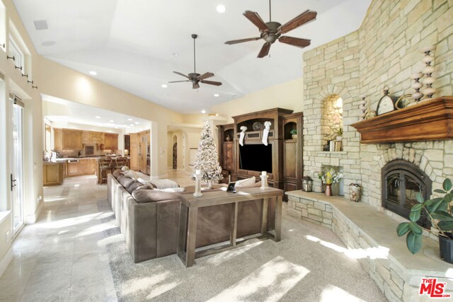 living room with ceiling fan, a stone fireplace, and vaulted ceiling