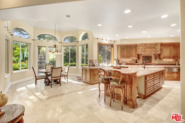 kitchen featuring kitchen peninsula, backsplash, a kitchen island with sink, hanging light fixtures, and light stone countertops