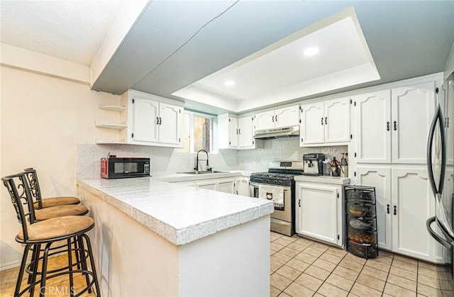 kitchen featuring kitchen peninsula, white cabinetry, sink, a tray ceiling, and stainless steel appliances