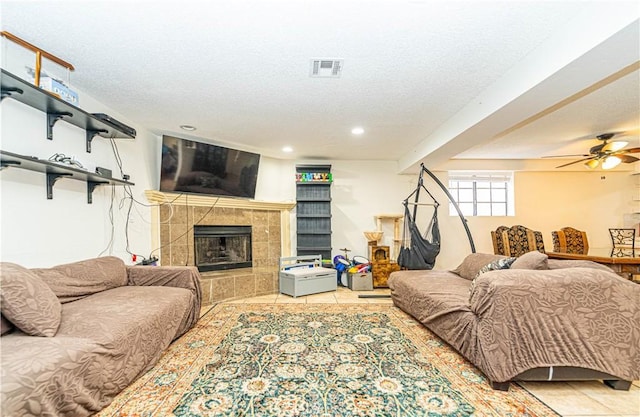 living room featuring a tiled fireplace, ceiling fan, light tile patterned floors, and a textured ceiling