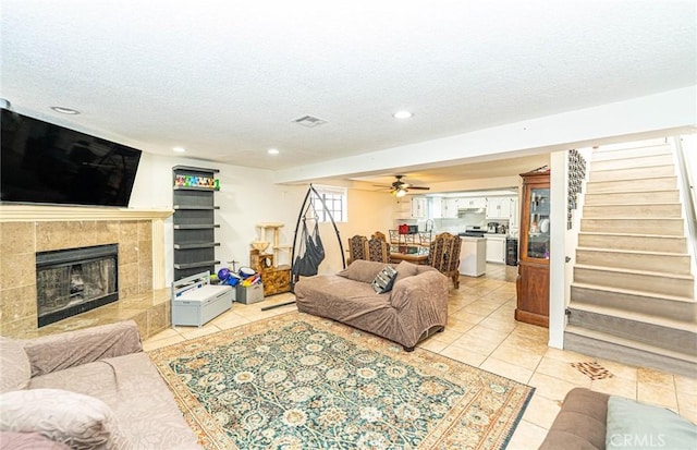 living room featuring light tile patterned floors, a tile fireplace, a textured ceiling, and ceiling fan