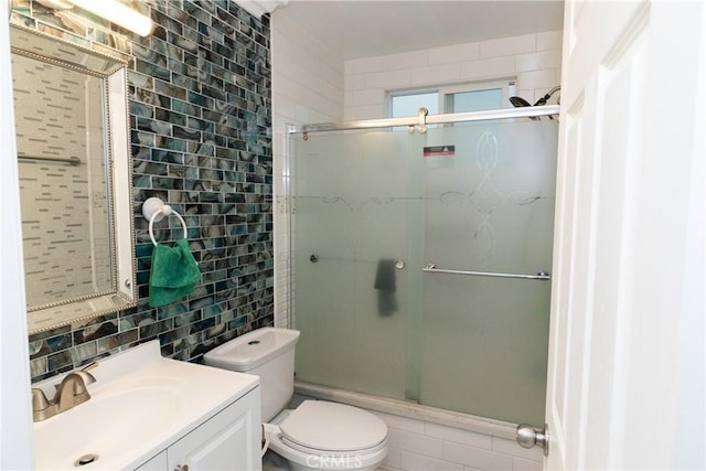 bathroom featuring toilet, vanity, a shower with door, and tasteful backsplash