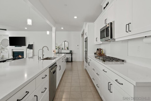 kitchen with appliances with stainless steel finishes, white cabinetry, sink, hanging light fixtures, and light tile patterned floors