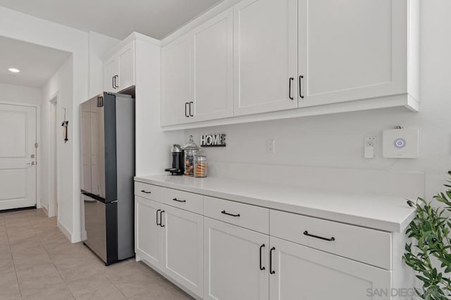 kitchen with light tile patterned floors, stainless steel fridge, and white cabinetry