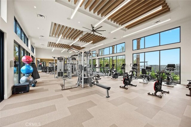 exercise room with light carpet, ceiling fan, and a towering ceiling