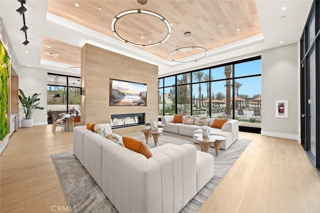 living room with baseboards, a fireplace, a raised ceiling, light wood-type flooring, and wooden ceiling