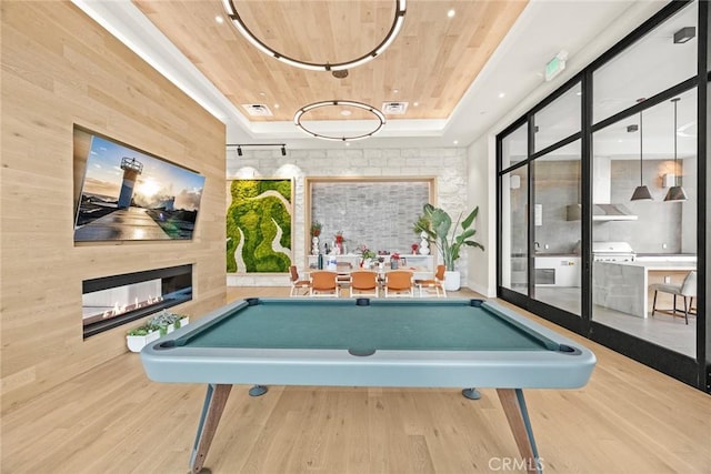 playroom featuring a multi sided fireplace, wood ceiling, a raised ceiling, and wood finished floors