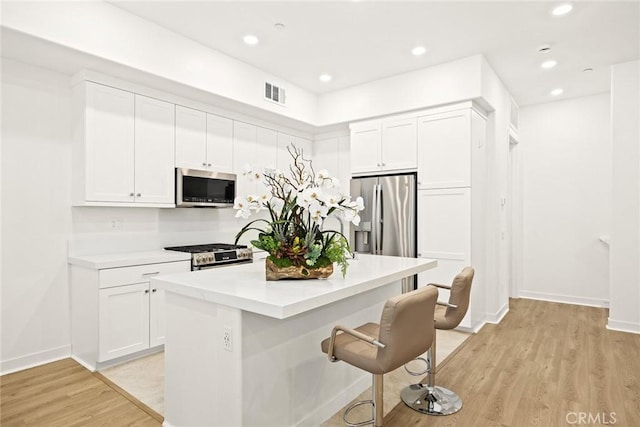 kitchen featuring white cabinets, appliances with stainless steel finishes, light hardwood / wood-style flooring, and a center island