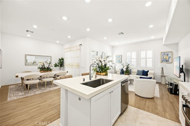 kitchen featuring dishwasher, a center island with sink, sink, white cabinetry, and light tile patterned floors