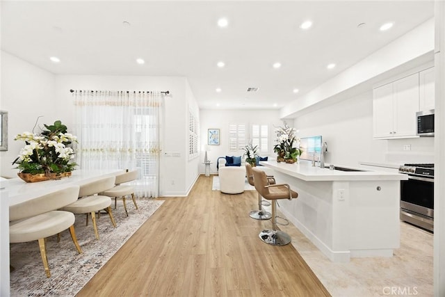 kitchen with white cabinetry, a center island with sink, stainless steel appliances, light hardwood / wood-style flooring, and sink