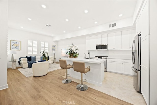 kitchen featuring white cabinets, stainless steel appliances, an island with sink, a kitchen breakfast bar, and light wood-type flooring