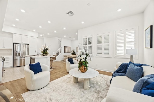 living room featuring stairs, light wood-type flooring, visible vents, and recessed lighting