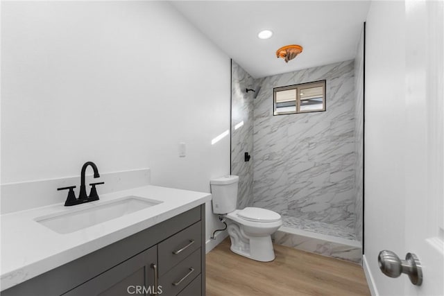 bathroom featuring toilet, a tile shower, wood-type flooring, and vanity