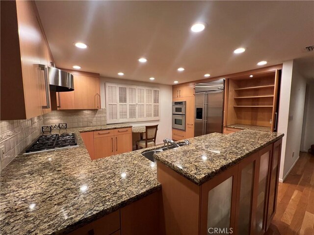 kitchen featuring kitchen peninsula, decorative backsplash, sink, appliances with stainless steel finishes, and wall chimney exhaust hood