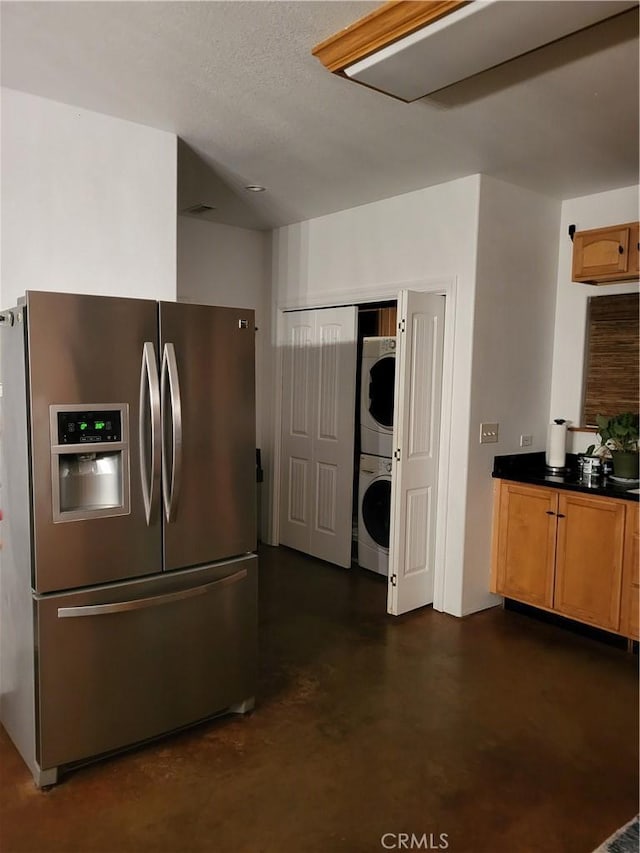 kitchen featuring stainless steel refrigerator with ice dispenser and stacked washer and dryer