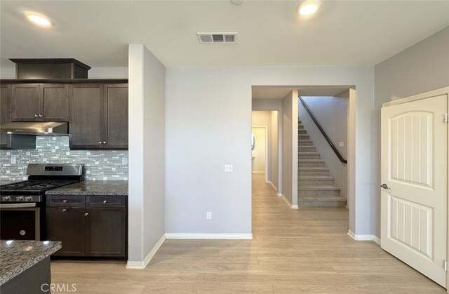 kitchen with stainless steel range with gas cooktop, backsplash, dark brown cabinets, and dark stone countertops