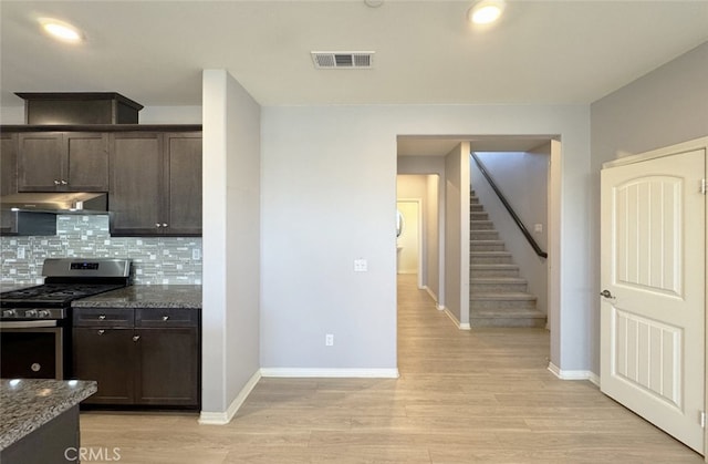 kitchen with stainless steel range with gas cooktop, dark brown cabinets, dark stone counters, and tasteful backsplash