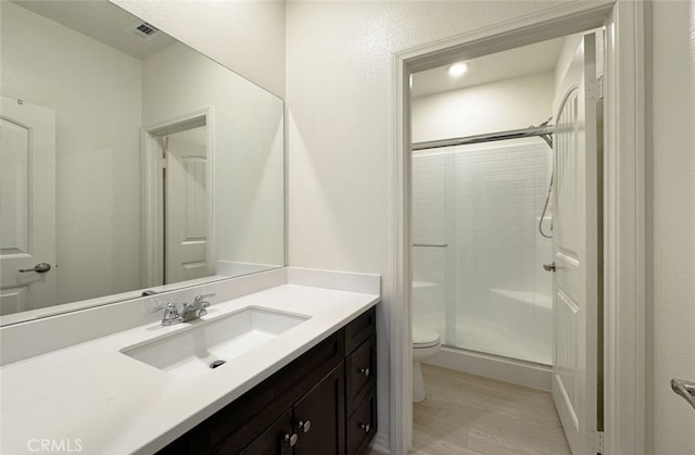 bathroom with toilet, a shower with shower door, wood-type flooring, and vanity