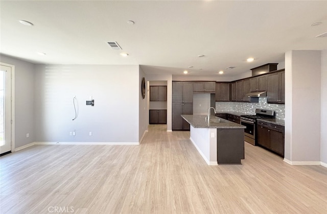 kitchen with backsplash, stainless steel range oven, light hardwood / wood-style floors, and a center island with sink