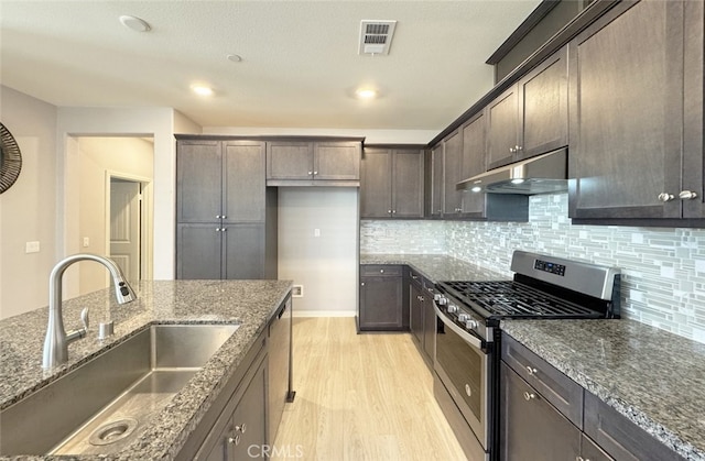 kitchen with stainless steel appliances, tasteful backsplash, dark stone counters, dark brown cabinetry, and sink