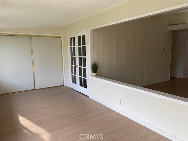 unfurnished room featuring a textured ceiling, french doors, and light wood-type flooring