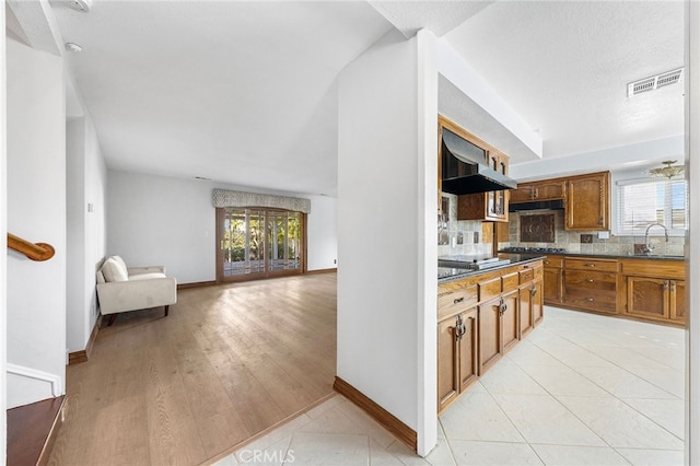 kitchen featuring sink, black stovetop, light tile patterned floors, decorative backsplash, and range hood