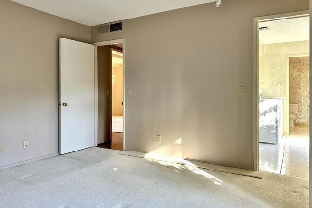 unfurnished bedroom with ensuite bath and light colored carpet