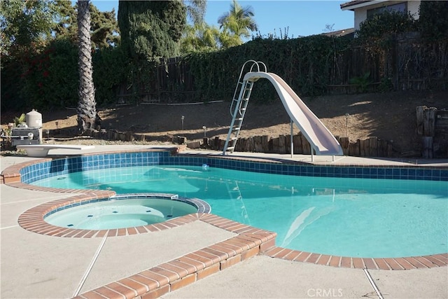 view of swimming pool featuring a pool with connected hot tub, a water slide, and a fenced backyard