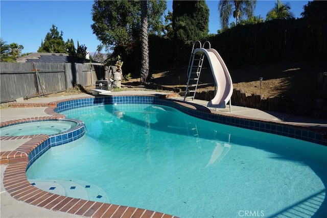 view of pool featuring a diving board, a water slide, a fenced backyard, and a pool with connected hot tub