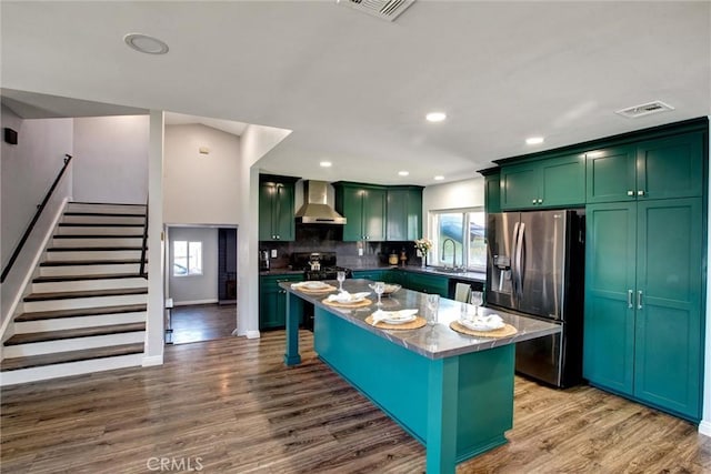 kitchen with visible vents, stainless steel refrigerator with ice dispenser, wood finished floors, wall chimney exhaust hood, and green cabinetry