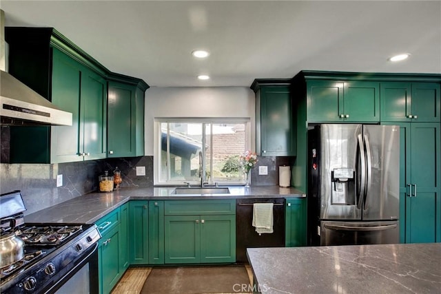 kitchen with a sink, range with gas cooktop, stainless steel fridge, wall chimney exhaust hood, and green cabinetry