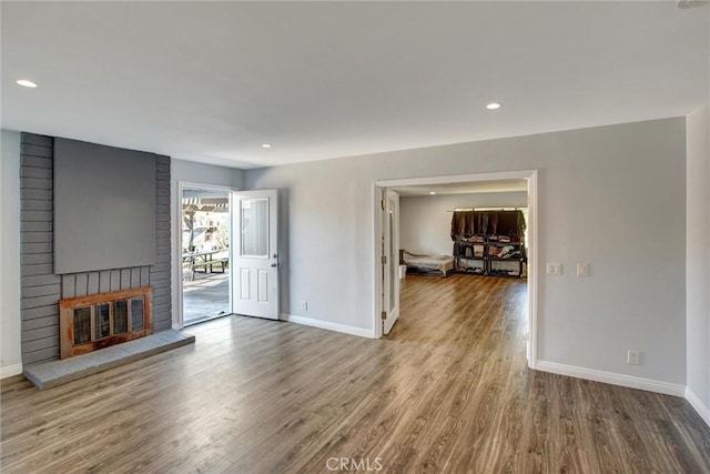 unfurnished living room with recessed lighting, baseboards, a brick fireplace, and wood finished floors