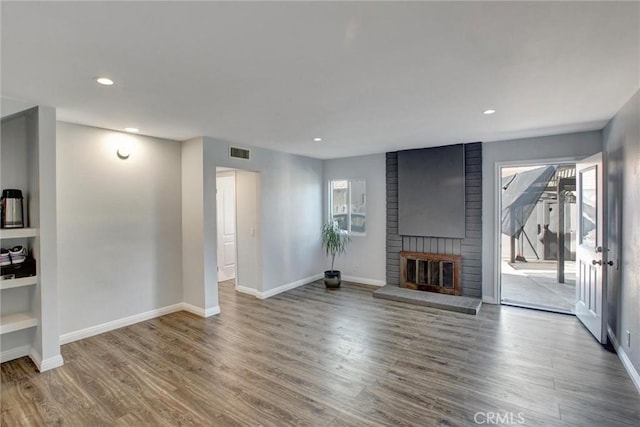 unfurnished living room featuring visible vents, baseboards, a brick fireplace, and wood finished floors