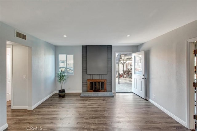 unfurnished living room with wood finished floors, a brick fireplace, a healthy amount of sunlight, and baseboards