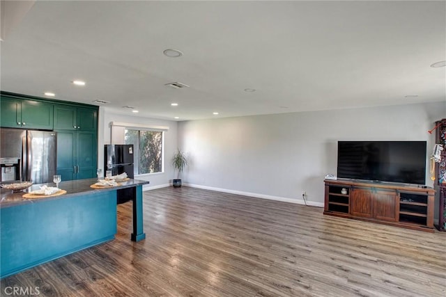 kitchen with stainless steel refrigerator with ice dispenser, wood finished floors, freestanding refrigerator, green cabinetry, and baseboards