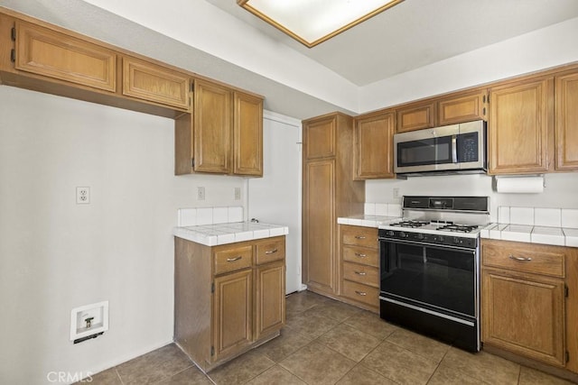 kitchen with light tile patterned floors, tile countertops, and gas stove