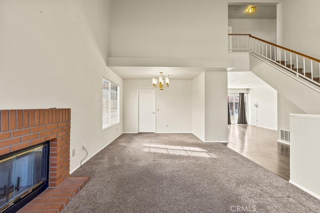 unfurnished living room featuring a fireplace, carpet, a chandelier, and a high ceiling