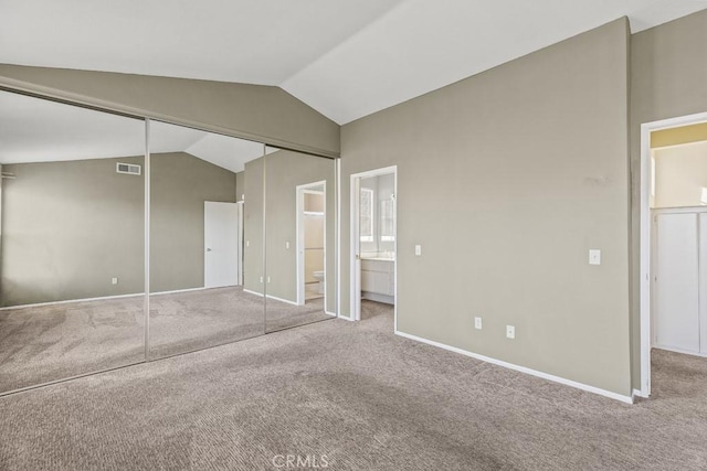 unfurnished bedroom with lofted ceiling, connected bathroom, a closet, and carpet