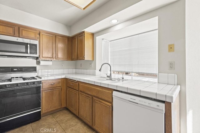 kitchen with sink, light tile patterned floors, dishwasher, tile counters, and gas range