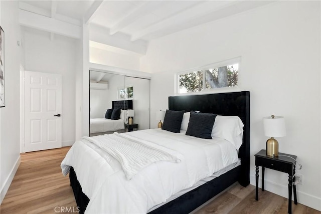 bedroom with beam ceiling, an AC wall unit, a closet, and hardwood / wood-style flooring