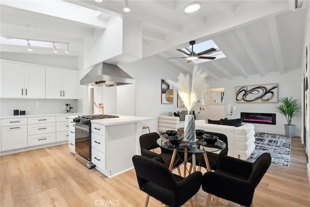 kitchen with lofted ceiling with beams, stainless steel range with gas cooktop, wall chimney range hood, and white cabinets