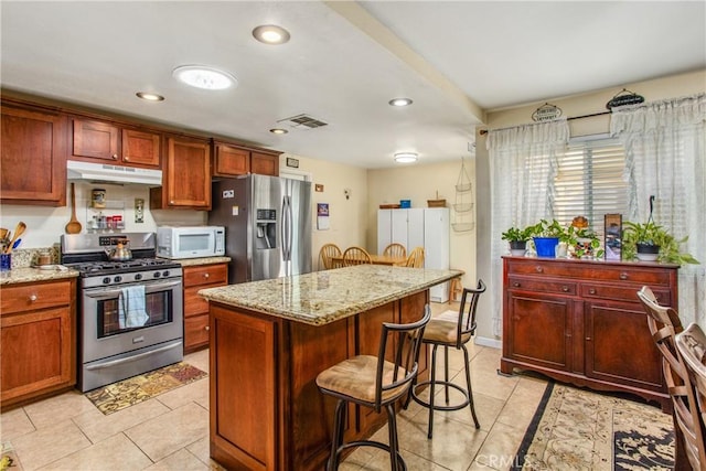 kitchen featuring light tile patterned floors, stainless steel appliances, light stone counters, and a kitchen island